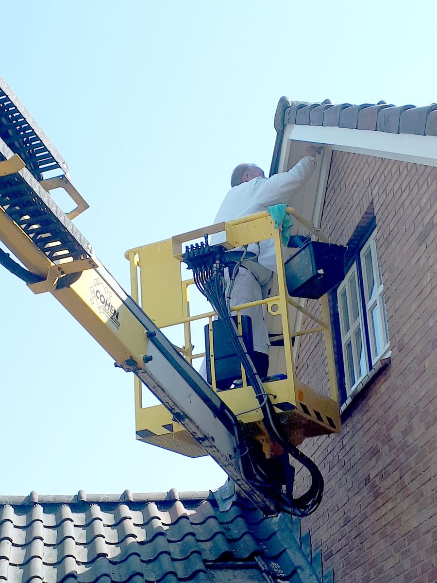 Gertjan schildert houtwerk onder een dakrand vanaf een hoogwerker